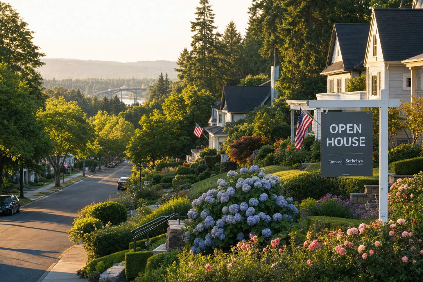 A tree-lined West Linn street at golden hour with an Open House sign in front of a craftsman home and the Willamette River bridge visible in the distance